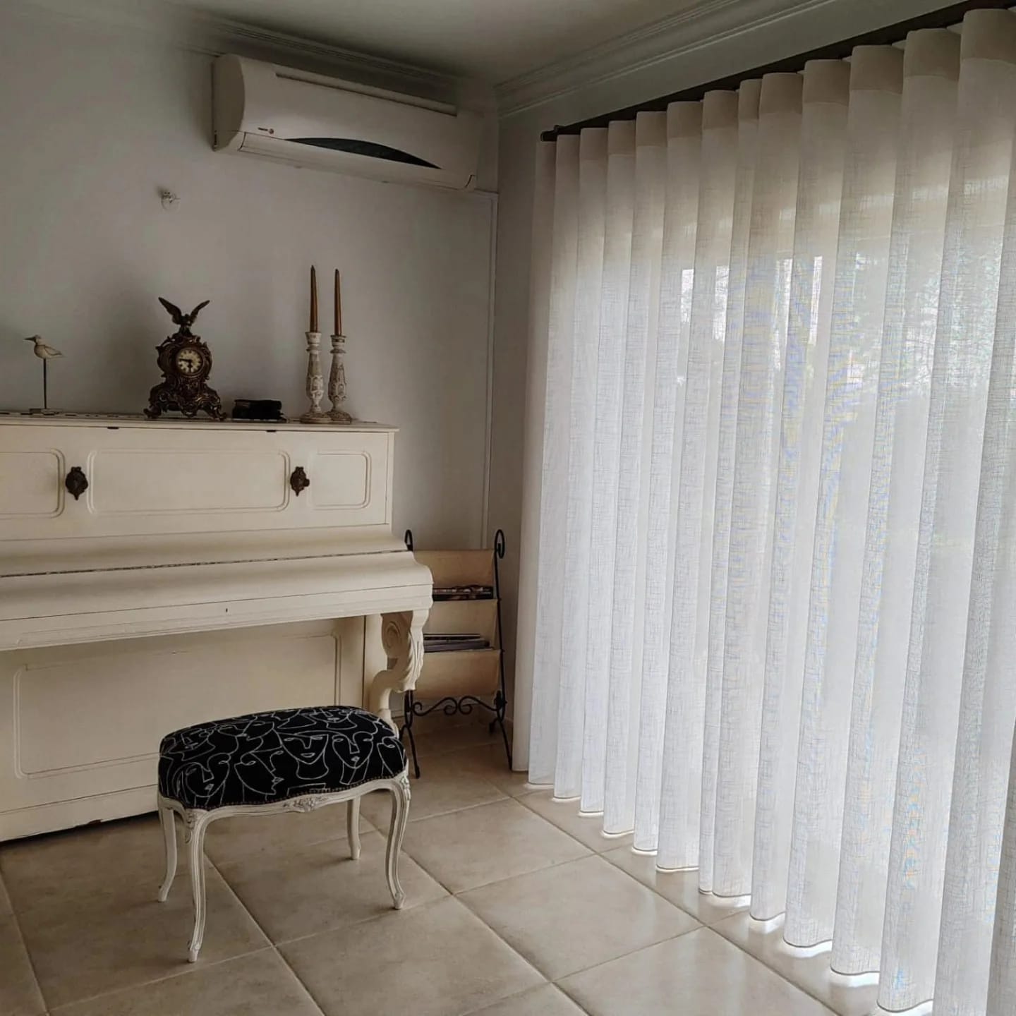 Sala com cortinado branco translúcido em onda a toda a largura da janela, junto a um piano