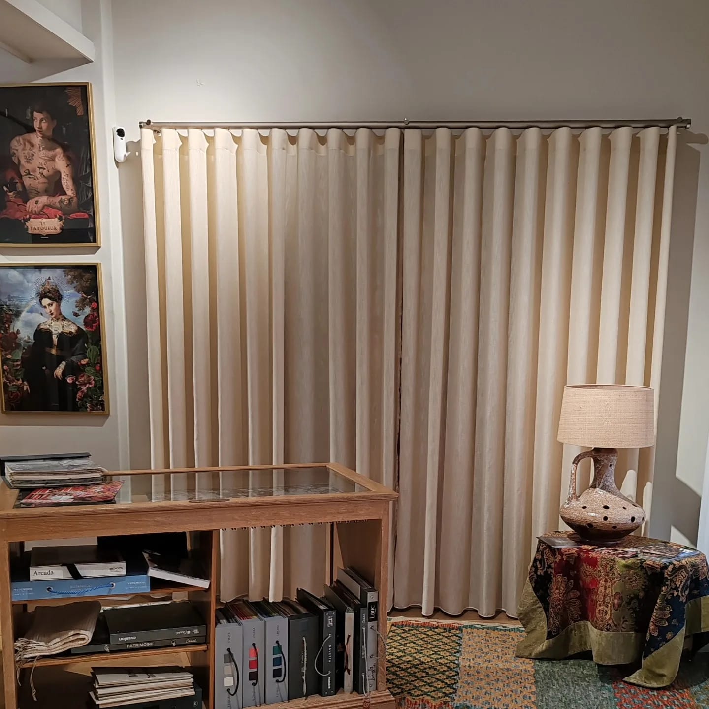 Showroom do Atelier Millet com cortinado cru em onda, vitrine com catálogos e candeeiro